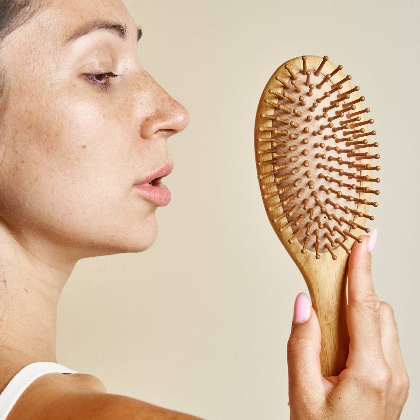 Person holding a wooden hairbrush against a neutral background