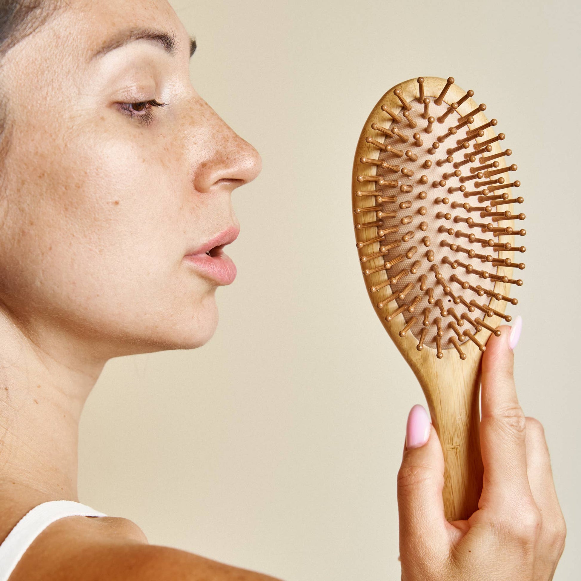 Person holding a wooden hairbrush against a neutral background