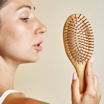 Person holding a wooden hairbrush against a neutral background