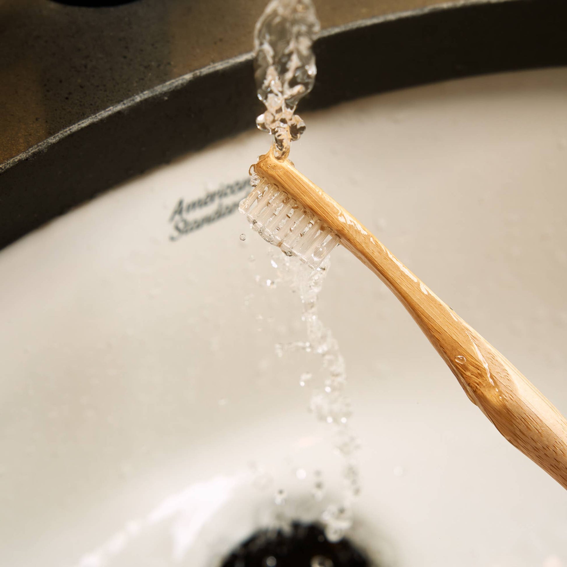 Wooden toothbrush with water droplets over a sink