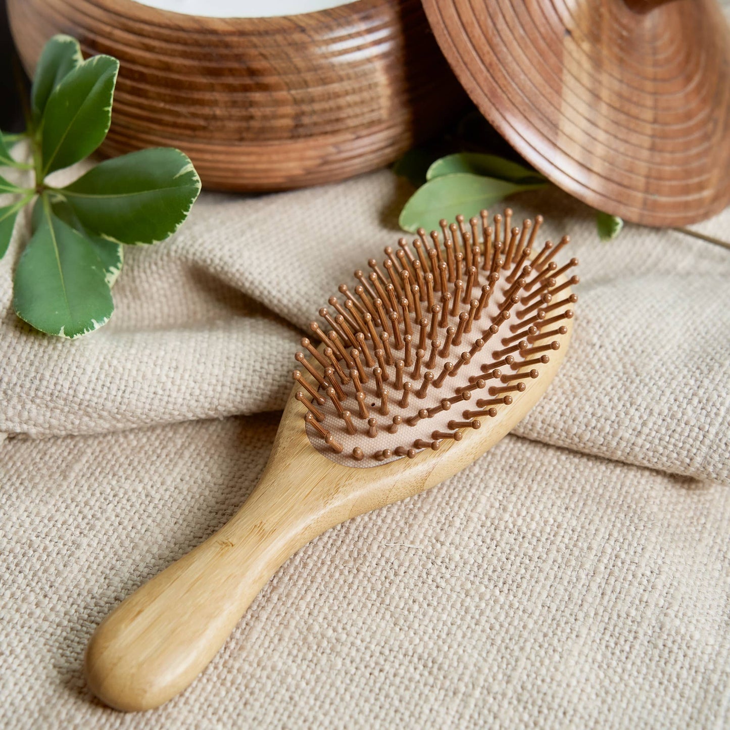 Wooden hairbrush on a textured fabric surface with green leaves.