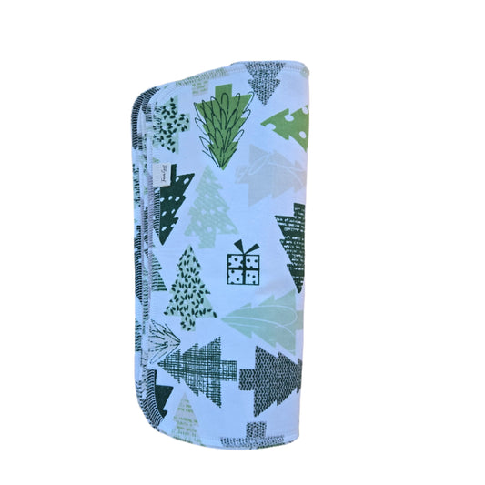 A white cotton towel with a multicolor geometric pattern featuring trees and a house, placed on a wooden surface.