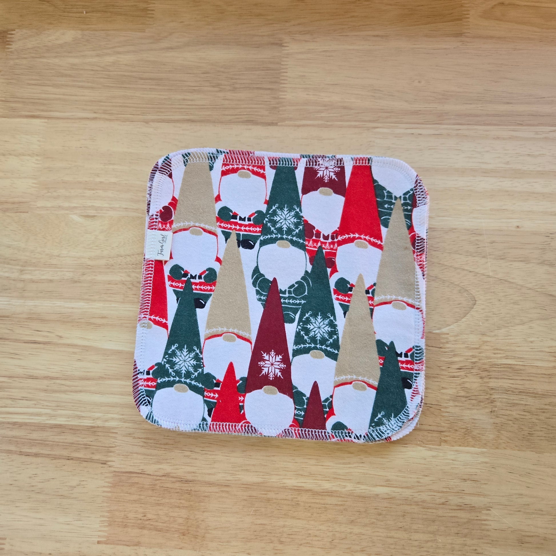 A multicolored cloth napkin with a Christmas-themed pattern, featuring snowflakes and gnomes, placed on a wooden surface.