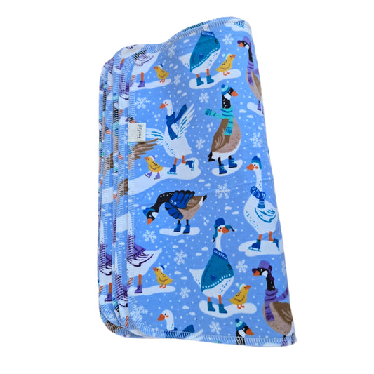 A folded blue paper towel with a winter-themed pattern featuring ice skating geese and snowflakes.