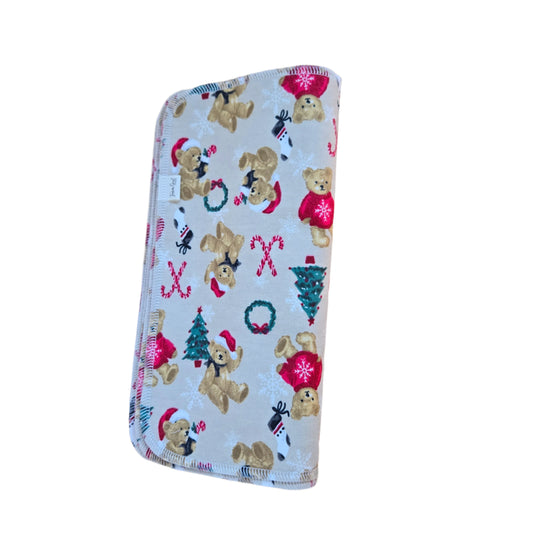 A square-shaped, multicolored paper towel with a teddy bear design, Christmas trees, and festive patterns, placed on a wooden surface.