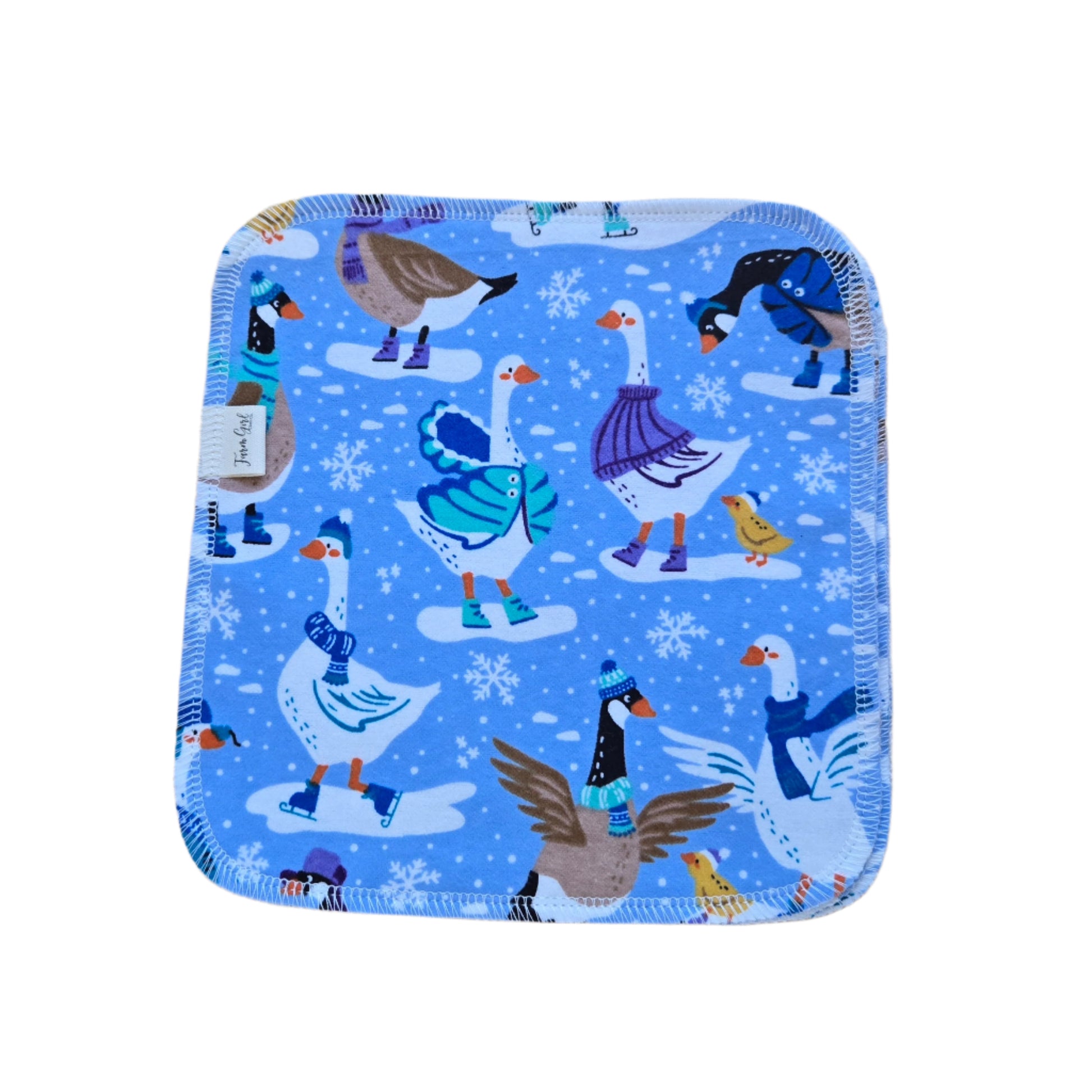 A cloth napkin with a pattern of ice skating geese and snowflakes on a blue background.