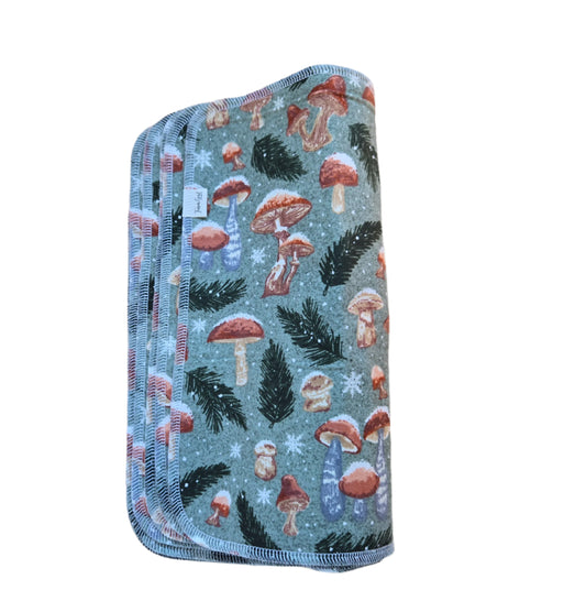 A set of folded paperless towels featuring a mushroom and pine design, placed on a wooden surface.