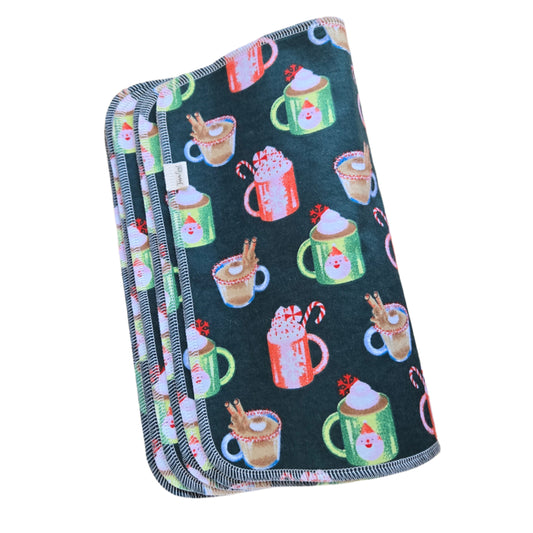 A stack of folded paperless towels with a Christmas-themed pattern including cups of coffee and candy canes on a dark background.