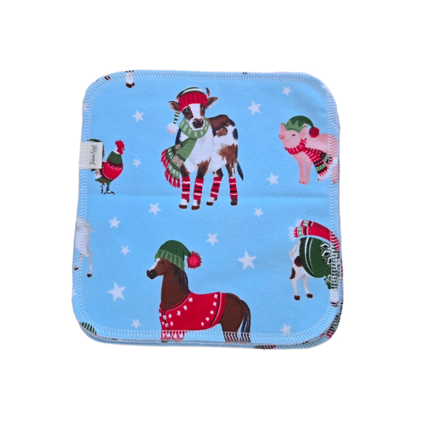 A blue cloth napkin with a winter farm animal theme, including depictions of a horse, cow, pig, and sheep, and decorated with Christmas-style hats and mittens.