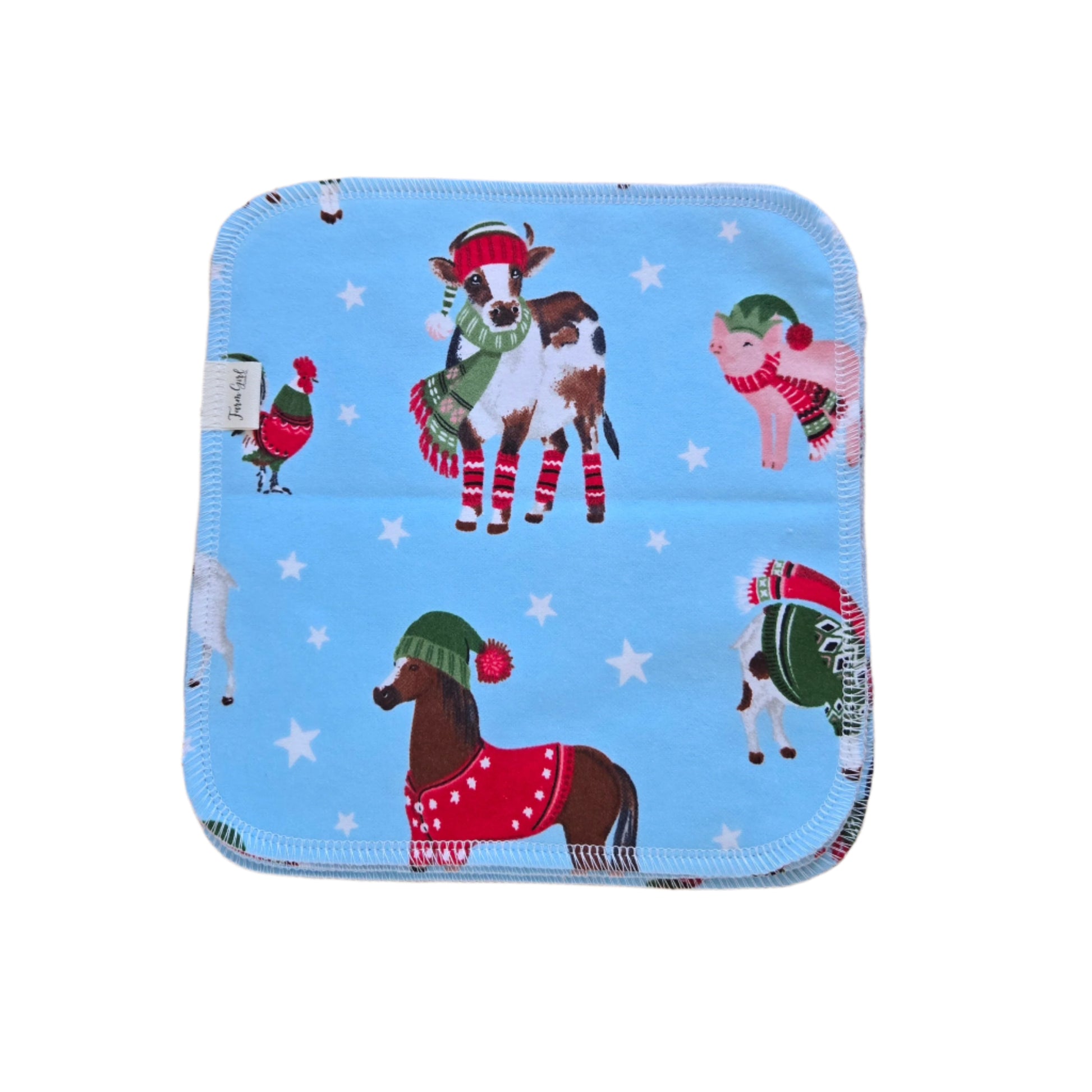 A blue cloth napkin with a winter farm animal theme, including depictions of a horse, cow, pig, and sheep, and decorated with Christmas-style hats and mittens.