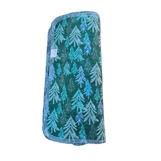 A square-shaped, green and blue paperless towel with a sparkling forest pattern, placed on a wooden surface.