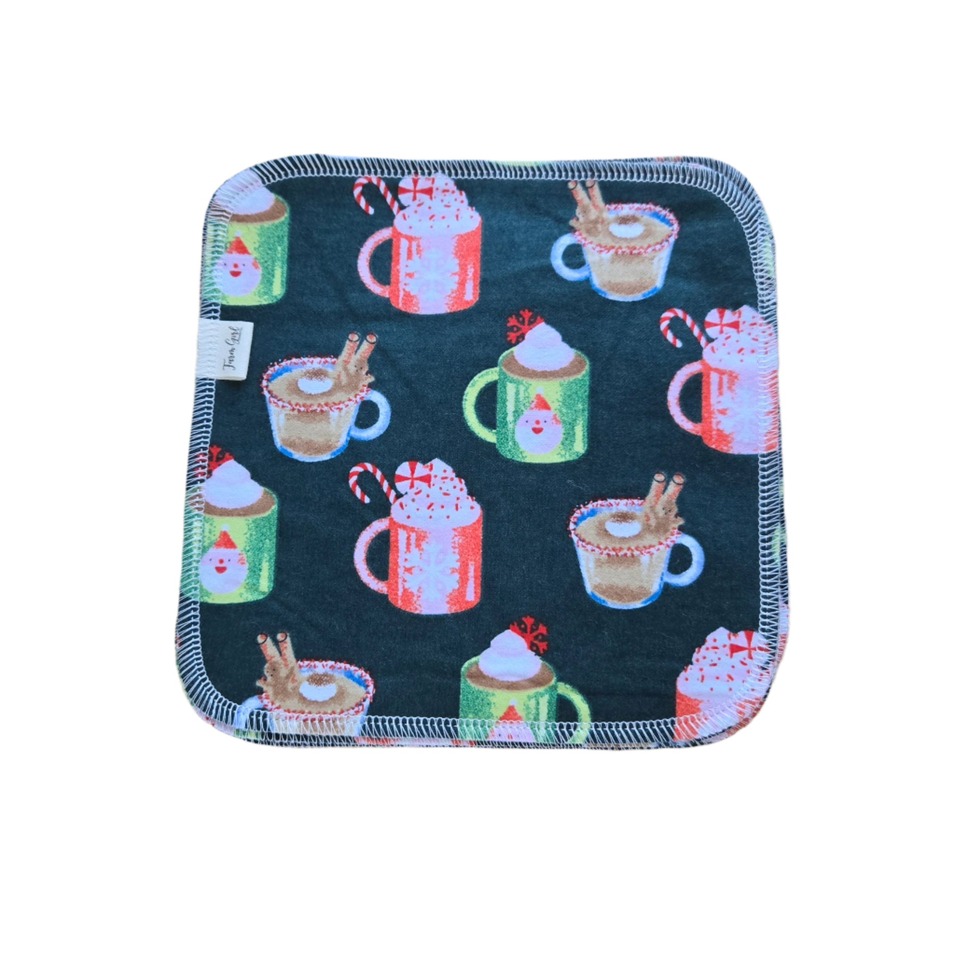 A multicolored cotton flannel cloth napkin with a pattern of Christmas-themed designs, including cups of cocoa and Santa Claus, placed on a wooden surface.
