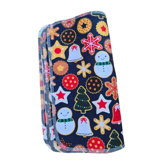 A folded towel with a Christmas-themed pattern including snowflakes, stars, and Christmas trees on a dark background, placed on a wooden surface.