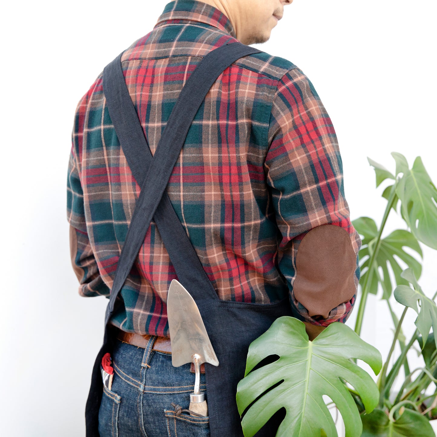 Photo of a man with a gardening shovel in his pocket, showing the back of the Linen crossback apron by farm girl cloth co.