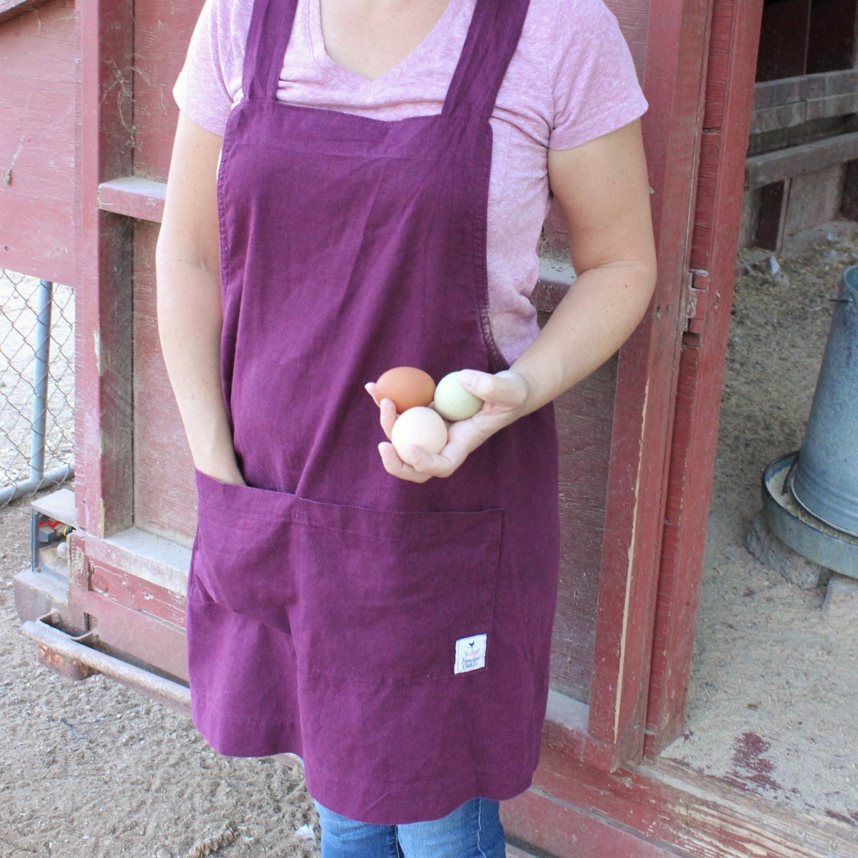 Photo of a woman holding chicken eggs wearing a plum colored linen apron by farm girl cloth co.
