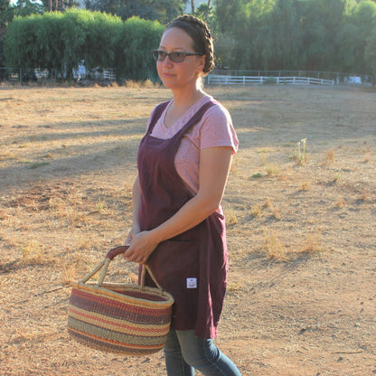 Photo of a woman with braids, standing in a field with a basket wearing a linen apron by Farm Girl Cloth Co.